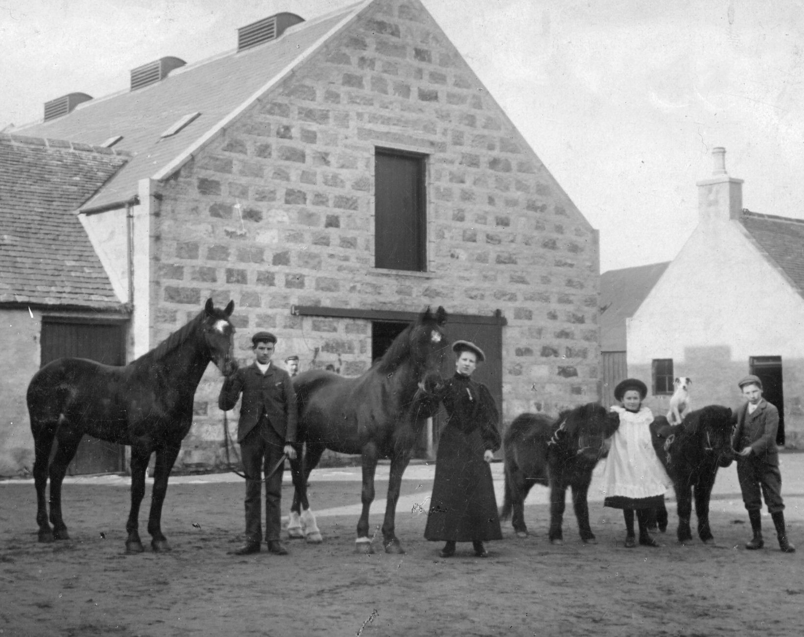 Four children with horses in front of stables